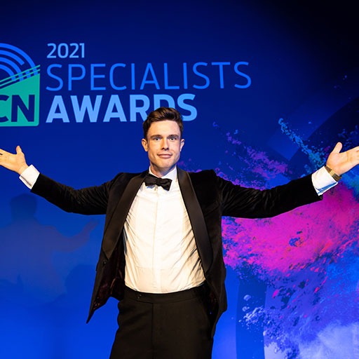 Ed Gamble, in a tuxedo, stands with arms outstretched on stage at the 2021 Specialists Awards.