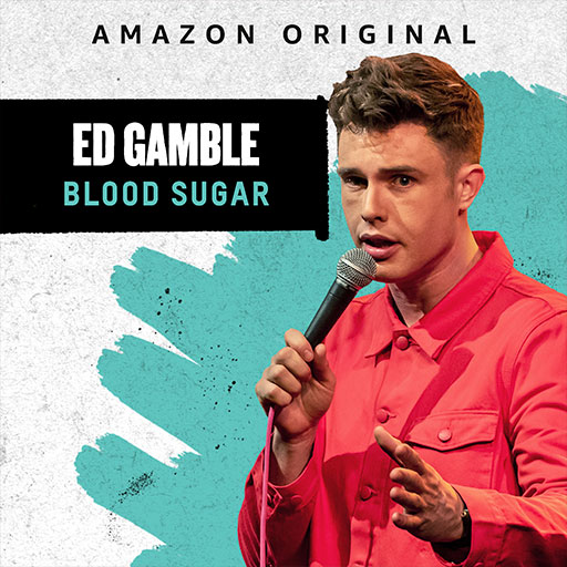 Ed Gamble, wearing a pink shirt, speaks into a microphone against a textured white and teal background.