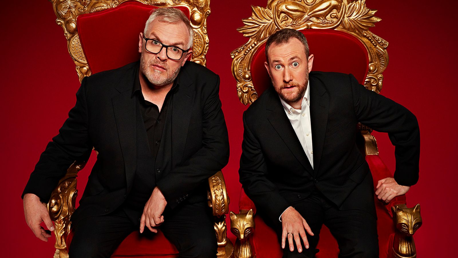 Alex Horne and Greg Davies seated on ornate golden thrones, wearing black suits against a red backdrop.