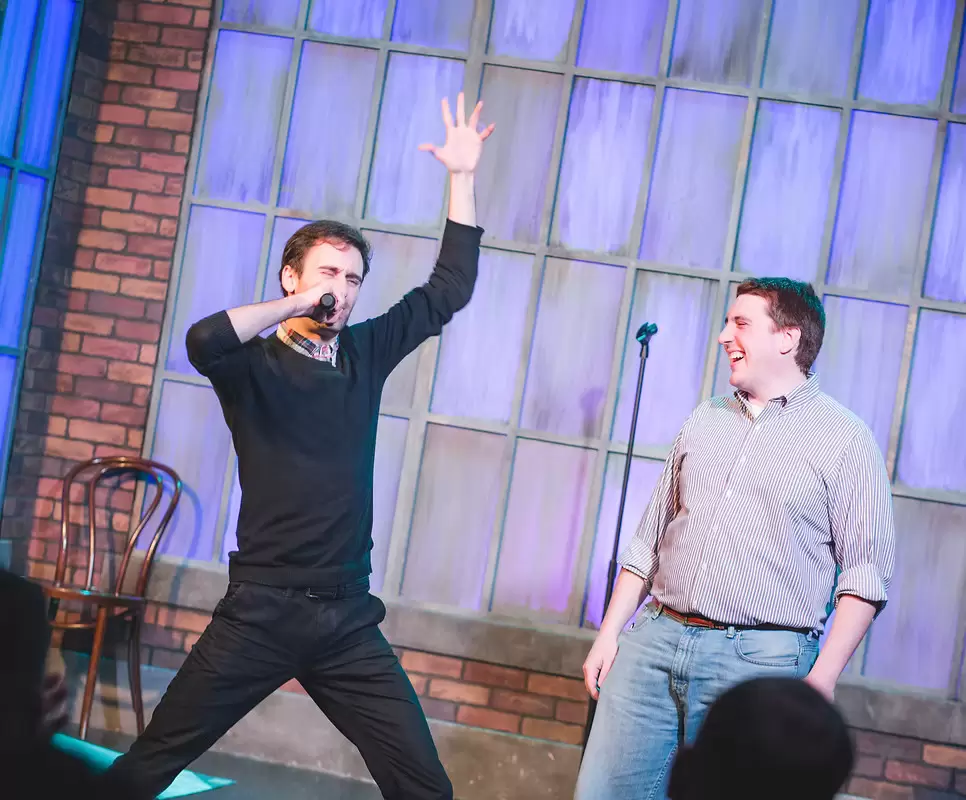 MC Hammersmith performs on stage, wearing a black shirt, with a microphone in hand and vibrant lighting.