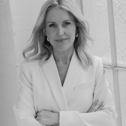 Jennifer Robinson stands confidently with arms crossed, wearing a white blazer against a light background.