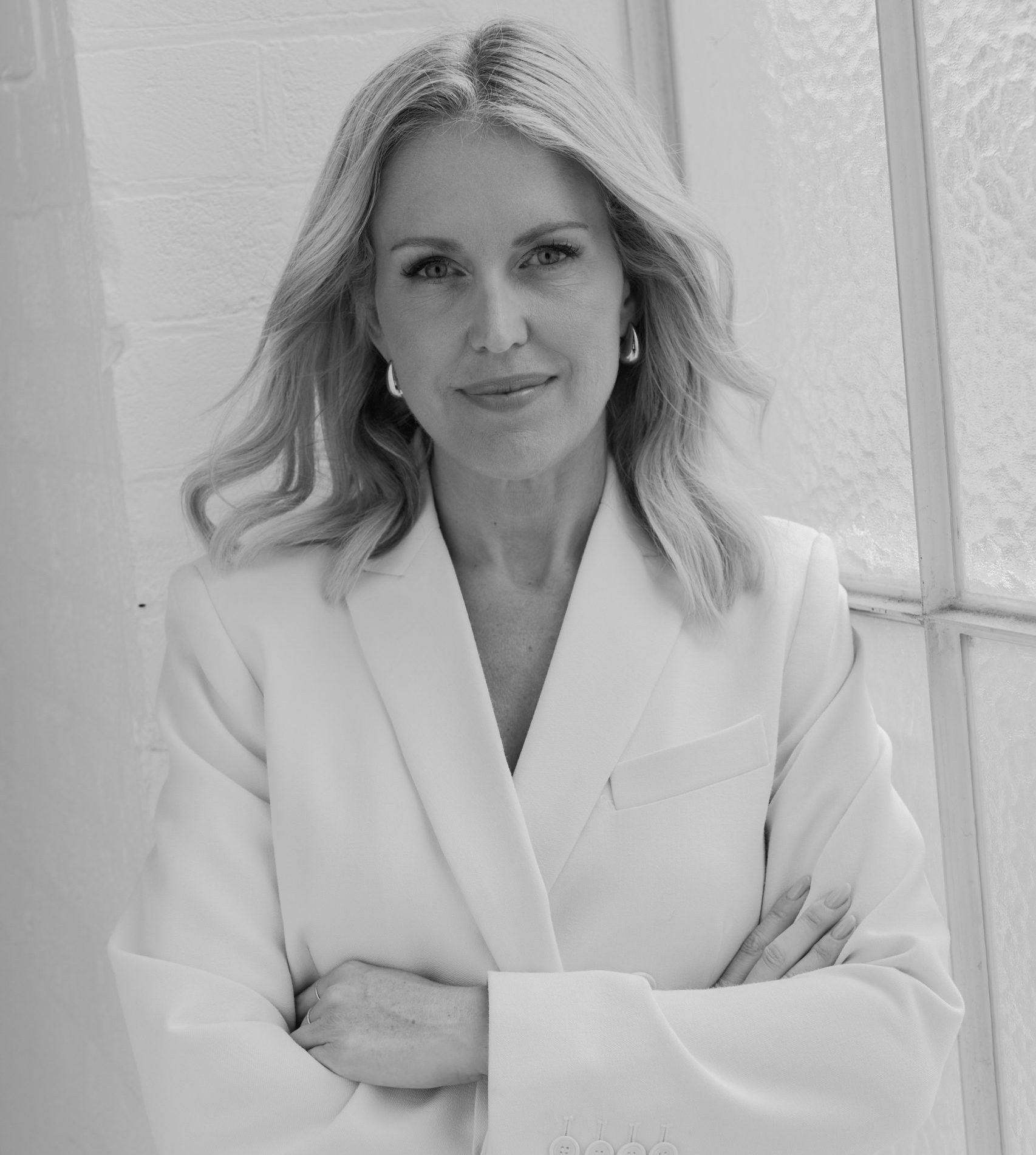 Jennifer Robinson stands confidently with arms crossed, wearing a white blazer against a light background.