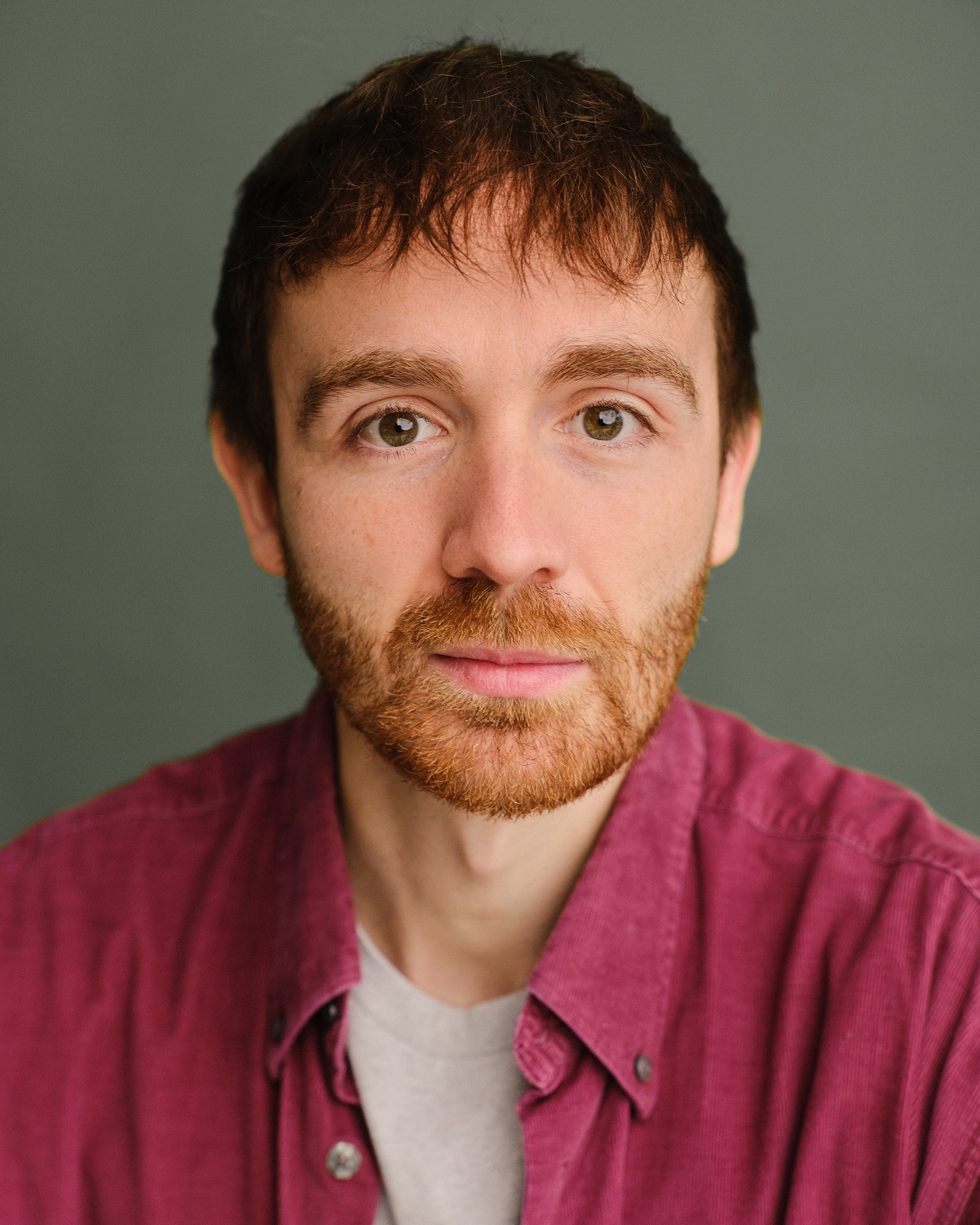 Ian Smith, with reddish-brown hair and beard, poses in a pink shirt against a grey background.